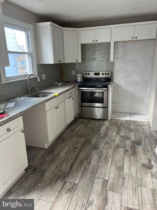 kitchen with wood finish floors, stainless steel electric stove, decorative backsplash, white cabinets, and a sink