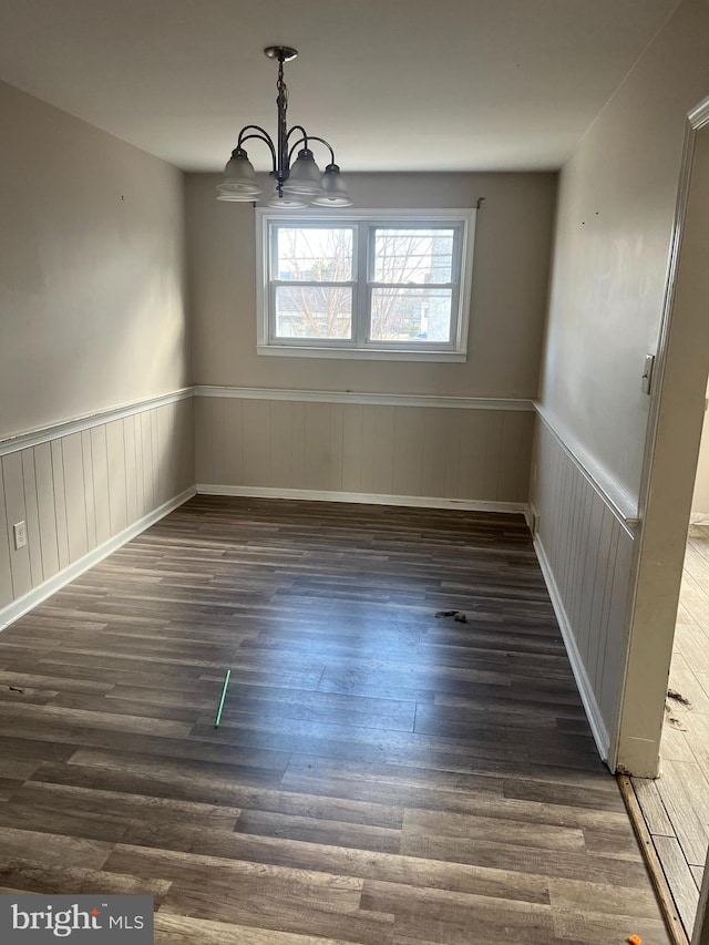 unfurnished dining area with wainscoting, wood finished floors, and a notable chandelier