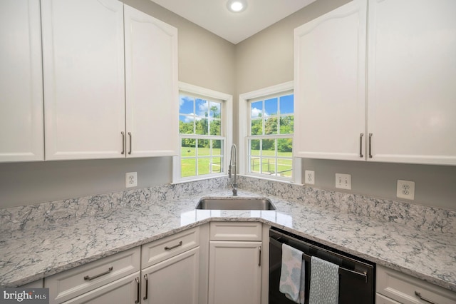 kitchen with light stone counters, black dishwasher, white cabinetry, and a sink