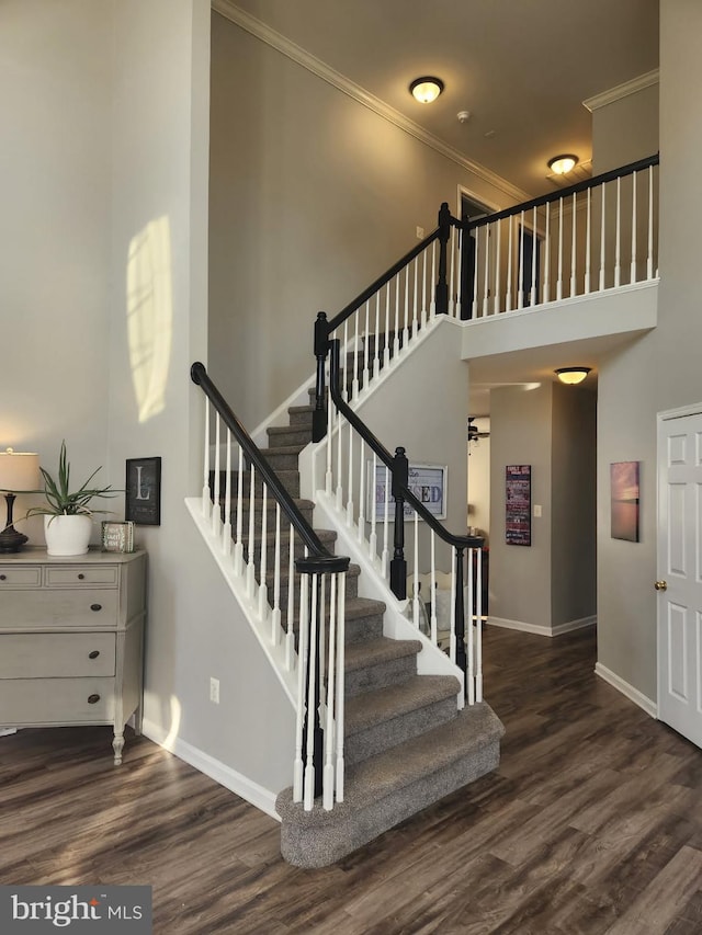 stairs with ornamental molding, wood finished floors, a high ceiling, and baseboards