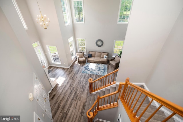 interior space featuring a notable chandelier, wood finished floors, a towering ceiling, baseboards, and stairway