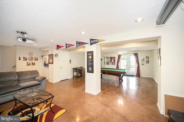 recreation room with french doors, finished concrete floors, an AC wall unit, a textured ceiling, and baseboards