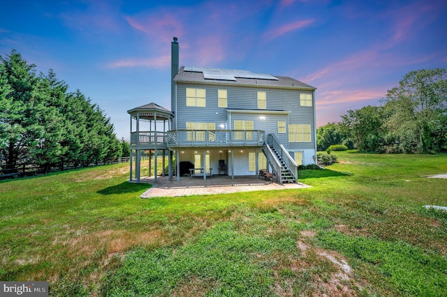 rear view of house featuring a patio, a chimney, solar panels, a wooden deck, and stairs