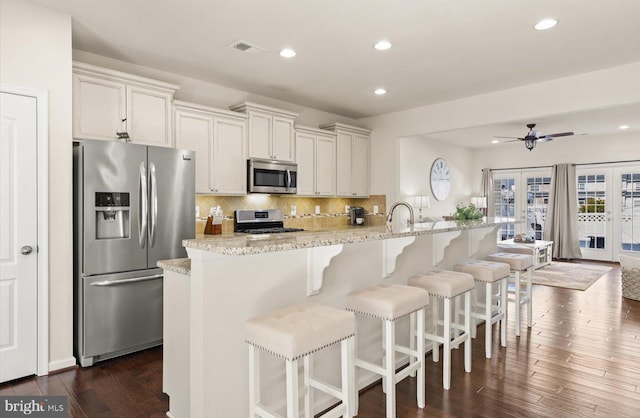 kitchen featuring visible vents, appliances with stainless steel finishes, a kitchen bar, backsplash, and dark wood finished floors