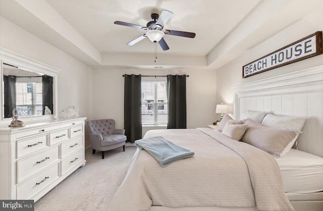 bedroom with light carpet, a tray ceiling, and a ceiling fan