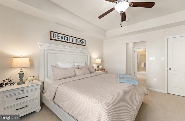 bedroom with a raised ceiling, light colored carpet, ensuite bathroom, a ceiling fan, and baseboards