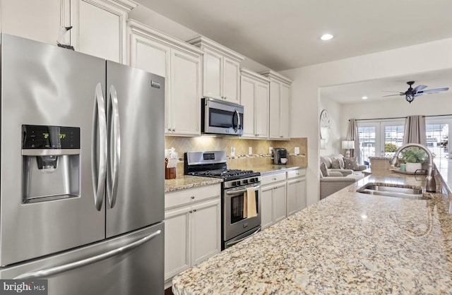 kitchen with light stone counters, appliances with stainless steel finishes, open floor plan, a sink, and backsplash