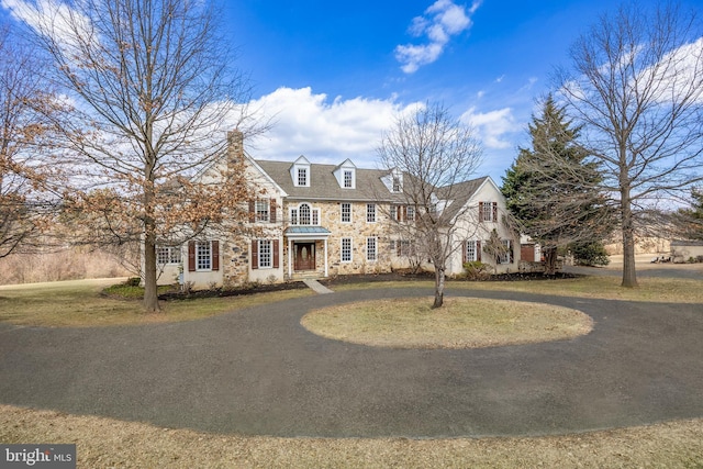 view of front of home featuring stone siding, curved driveway, and a front lawn