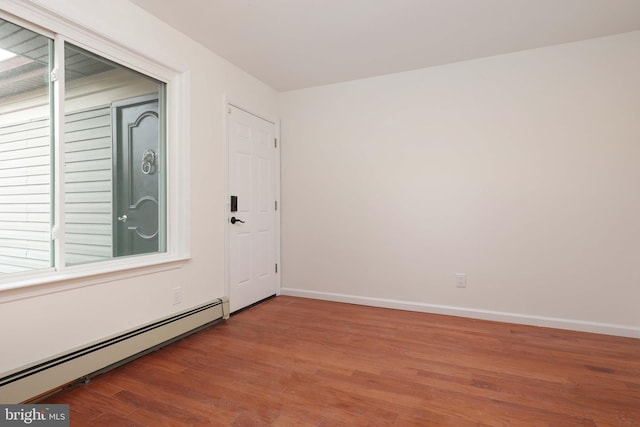 empty room with a baseboard heating unit, wood finished floors, and baseboards