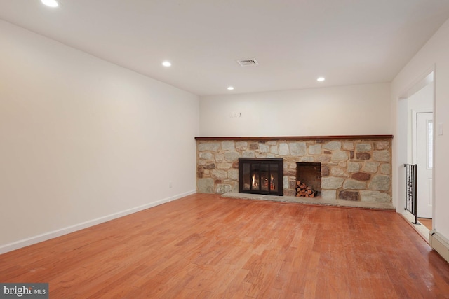 unfurnished living room featuring recessed lighting, baseboards, wood finished floors, and a stone fireplace