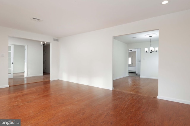 empty room featuring recessed lighting, visible vents, wood finished floors, a chandelier, and baseboards