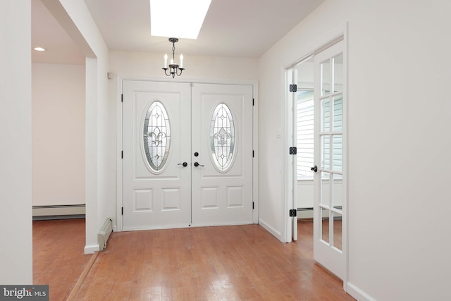 entryway featuring french doors, a notable chandelier, light wood finished floors, a baseboard radiator, and baseboards