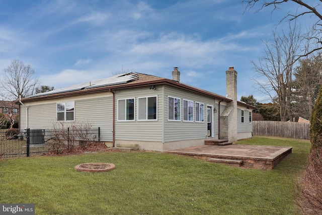 back of property with a chimney, solar panels, a lawn, a patio area, and fence