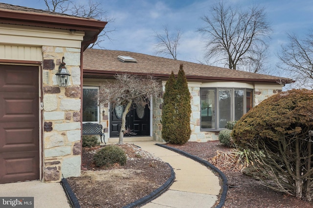 doorway to property with a garage, stone siding, and roof with shingles