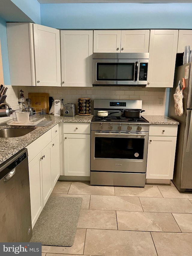 kitchen featuring light tile patterned floors, tasteful backsplash, appliances with stainless steel finishes, white cabinets, and a sink