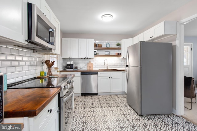 kitchen featuring backsplash, appliances with stainless steel finishes, white cabinetry, a sink, and wood counters