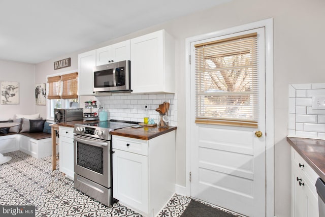 kitchen with appliances with stainless steel finishes, butcher block countertops, white cabinetry, and tasteful backsplash