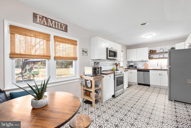 kitchen featuring white cabinets, appliances with stainless steel finishes, a sink, open shelves, and backsplash