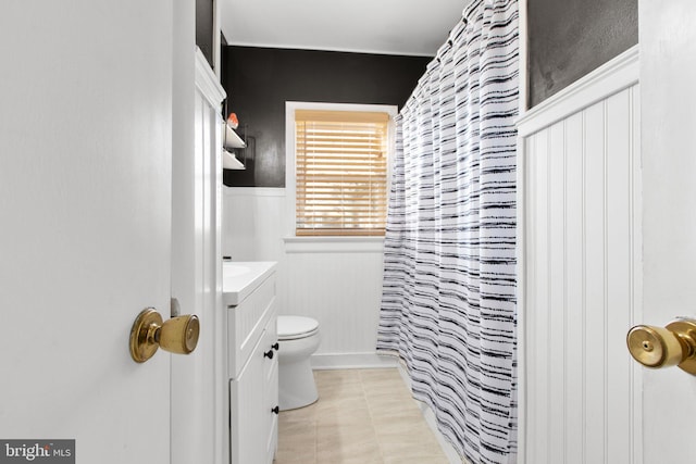 bathroom with a shower with shower curtain, wainscoting, vanity, and toilet