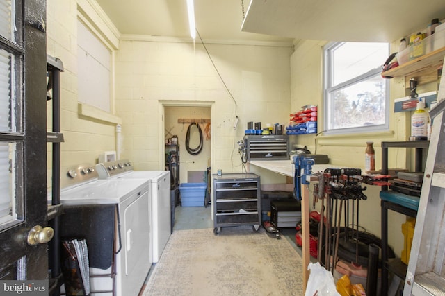 clothes washing area with laundry area, a workshop area, washing machine and clothes dryer, and concrete block wall