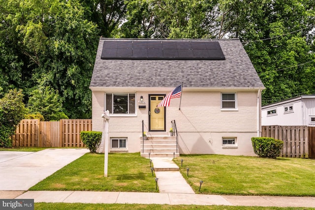 view of front of house with a front yard, roof mounted solar panels, brick siding, and roof with shingles