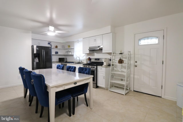 kitchen featuring open shelves, white cabinetry, under cabinet range hood, stainless steel gas range oven, and black fridge