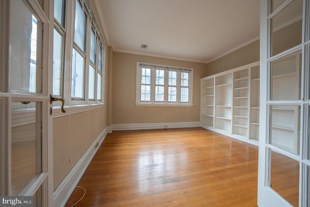 empty room with plenty of natural light, visible vents, crown molding, and light wood finished floors