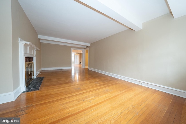 unfurnished living room featuring a chandelier, a glass covered fireplace, beam ceiling, and light wood-style flooring