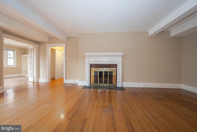 unfurnished living room featuring hardwood / wood-style floors, a brick fireplace, beam ceiling, and baseboards