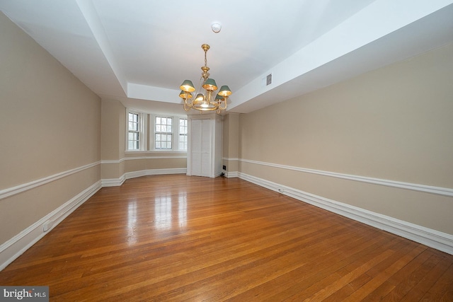 empty room with a tray ceiling, visible vents, an inviting chandelier, light wood-type flooring, and baseboards