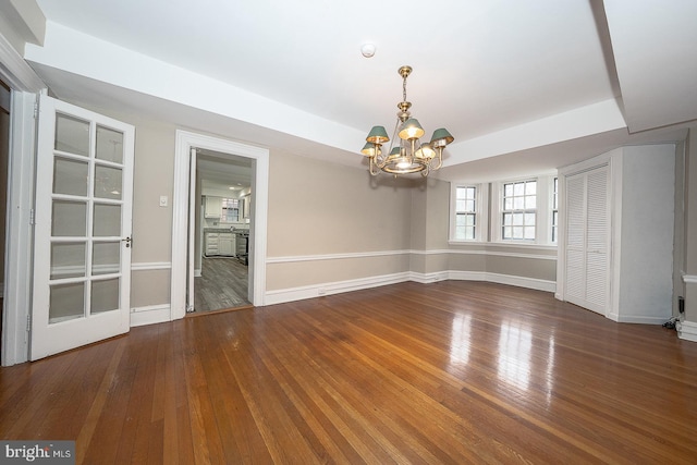 spare room with a raised ceiling, baseboards, hardwood / wood-style floors, and an inviting chandelier