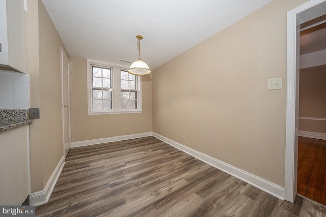 unfurnished dining area with dark wood-style flooring and baseboards