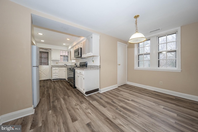 kitchen featuring black range with gas cooktop, visible vents, stainless steel microwave, freestanding refrigerator, and white cabinetry