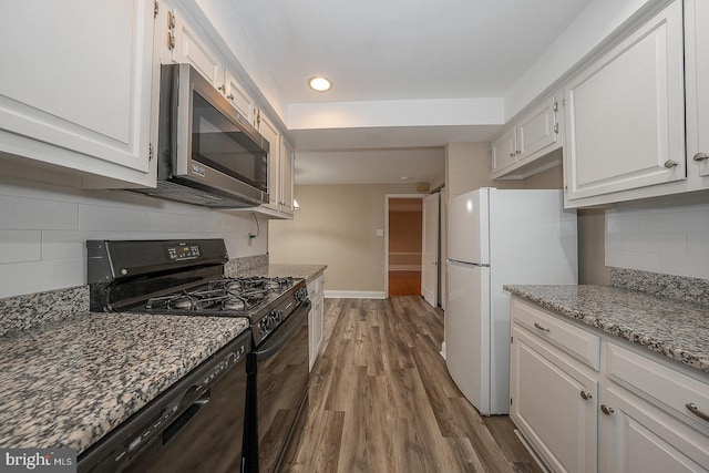 kitchen featuring black appliances, dark stone countertops, white cabinetry, and wood finished floors