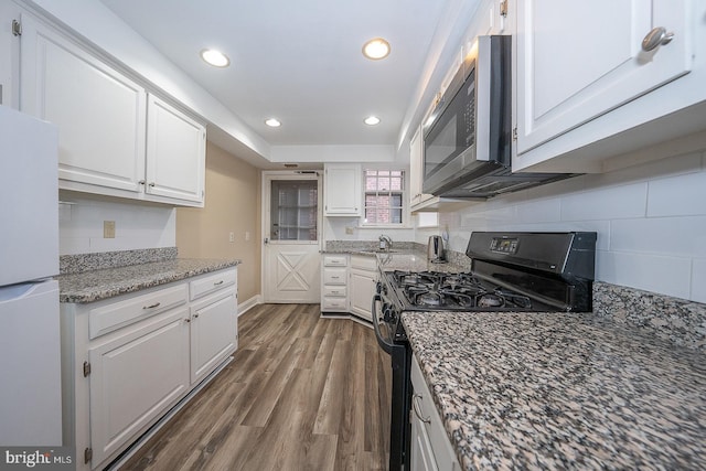 kitchen featuring stainless steel microwave, freestanding refrigerator, white cabinetry, black gas stove, and a sink