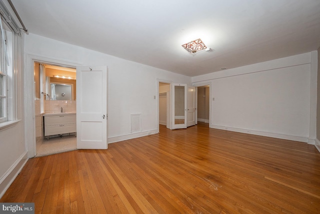 unfurnished bedroom with ensuite bathroom, light wood finished floors, a sink, and baseboards