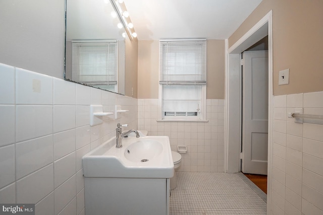 half bath with toilet, tile patterned floors, tile walls, and vanity