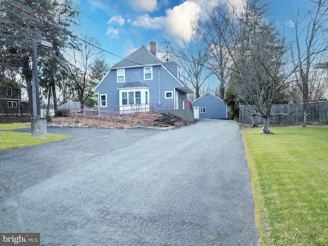 exterior space featuring a shingled roof, fence, driveway, a front lawn, and a chimney