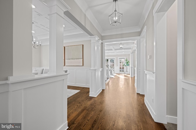 hall featuring ornamental molding, a chandelier, a decorative wall, and ornate columns