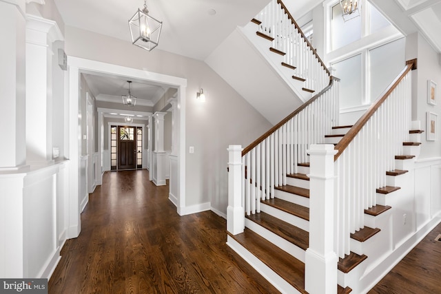 foyer with a decorative wall, wood finished floors, wainscoting, decorative columns, and an inviting chandelier