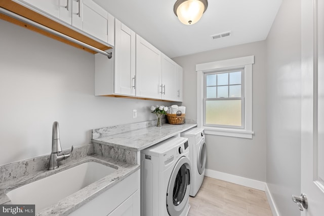 clothes washing area featuring separate washer and dryer, a sink, visible vents, baseboards, and cabinet space