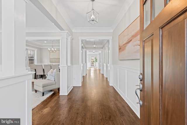 foyer with decorative columns, dark wood-style floors, crown molding, a chandelier, and a decorative wall