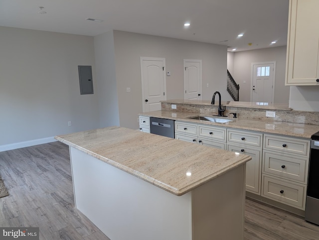 kitchen featuring electric panel, a sink, wood finished floors, a peninsula, and stainless steel dishwasher