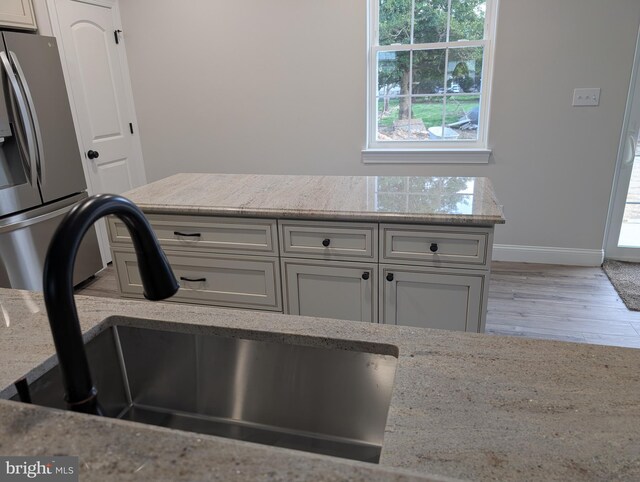 kitchen featuring light stone countertops, a sink, stainless steel fridge with ice dispenser, and a healthy amount of sunlight