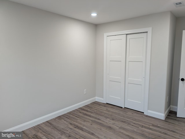 unfurnished bedroom with a closet, wood finished floors, baseboards, visible vents, and recessed lighting