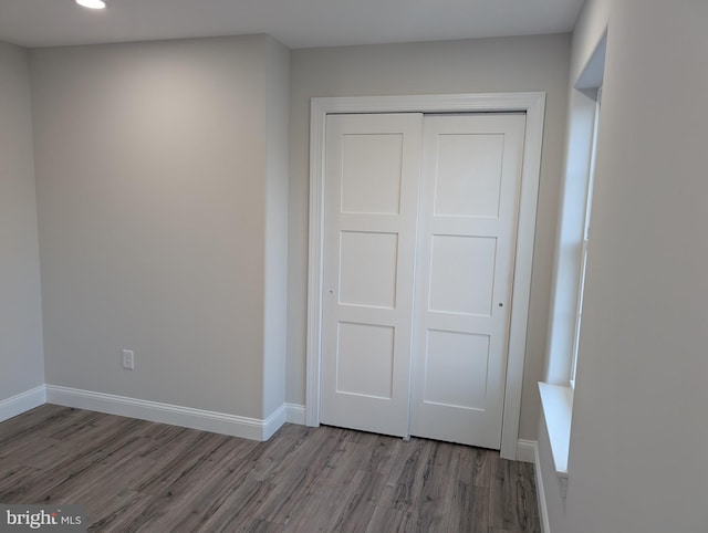 unfurnished bedroom featuring baseboards, recessed lighting, wood finished floors, and a closet