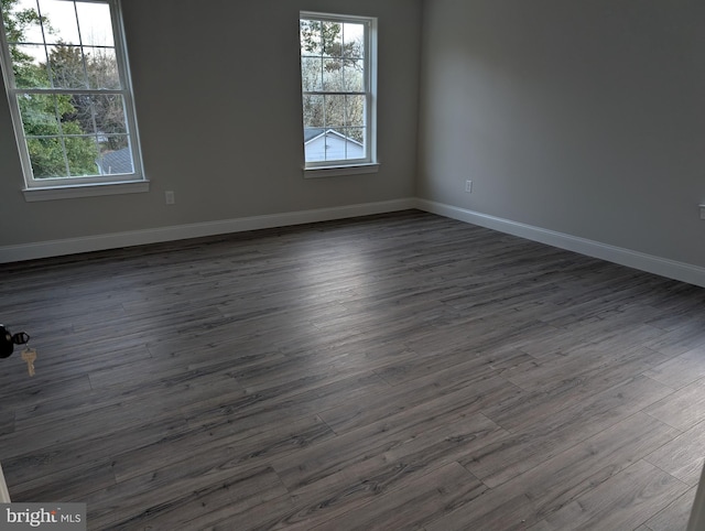 spare room featuring plenty of natural light, baseboards, and dark wood-style flooring