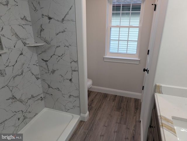 bathroom featuring a shower, baseboards, wood finished floors, toilet, and vanity