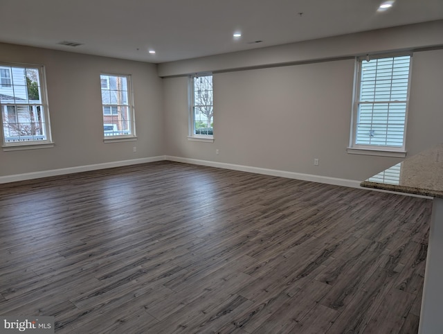 empty room featuring dark wood-style flooring, visible vents, baseboards, and recessed lighting