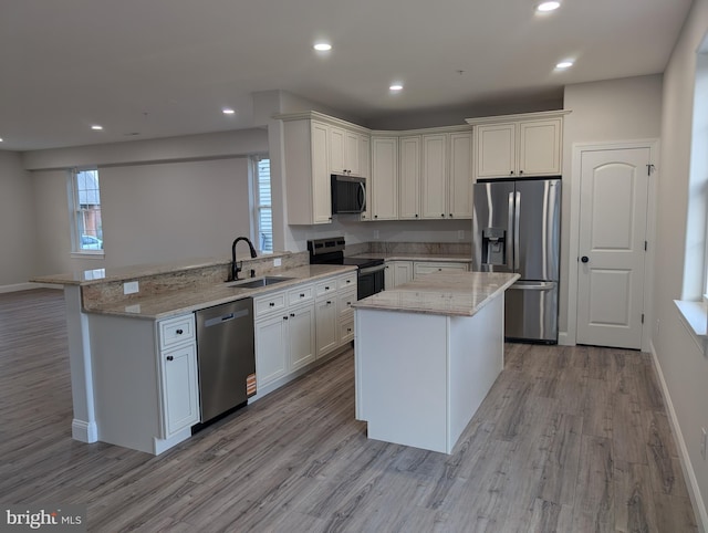 kitchen featuring a peninsula, stainless steel appliances, a sink, light wood-style floors, and light stone counters